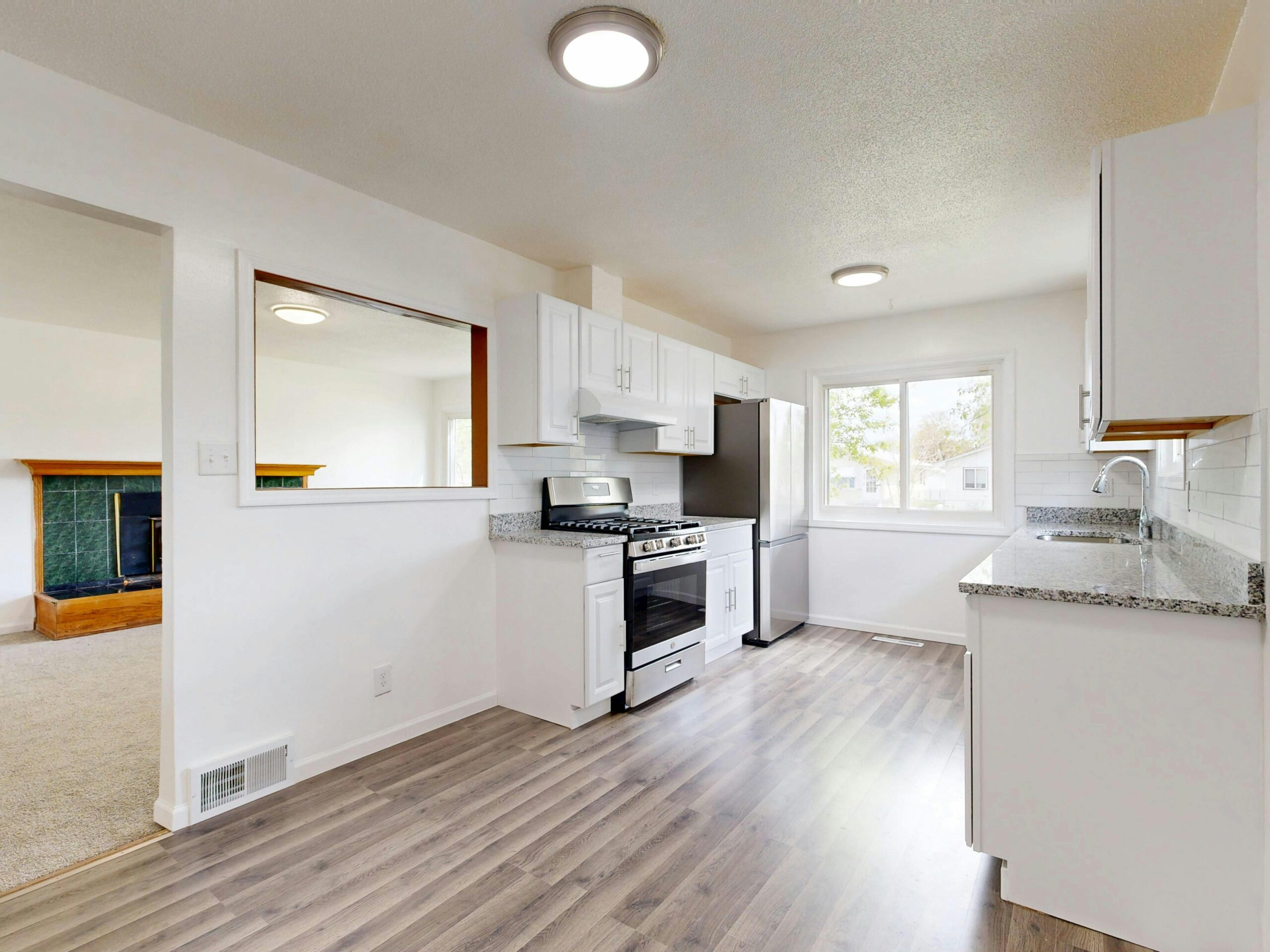 Bright, newly renovated kitchen featuring white cabinets, hardwood floors, and stainless steel appliances.